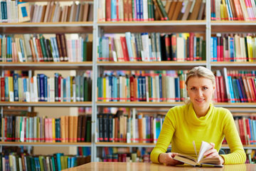a student sitting at a library table, holding an open book